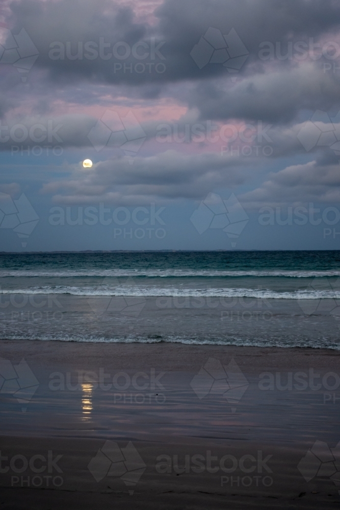 Moon reflected on the sand as it rises over the beach at sunset - Australian Stock Image