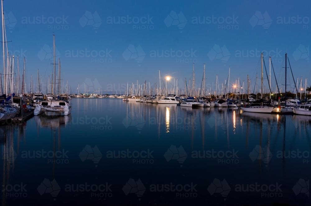 Moon rising over yachts in marina with reflections in water - Australian Stock Image