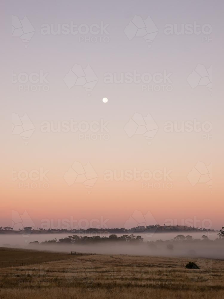 Moon setting over fog at dawn - Australian Stock Image