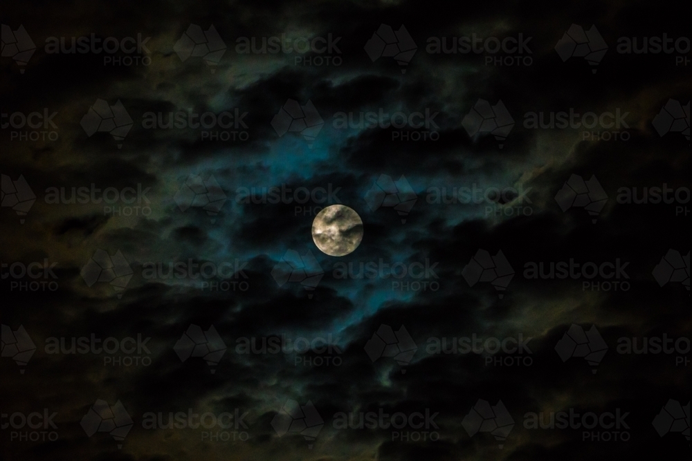 Moon with blue and white light covered with clouds - Australian Stock Image
