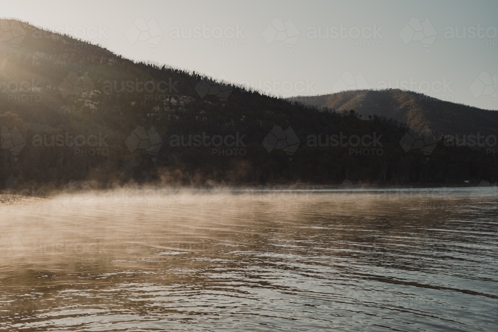 Morning fog lit up by the sun with mountains in the background - Australian Stock Image