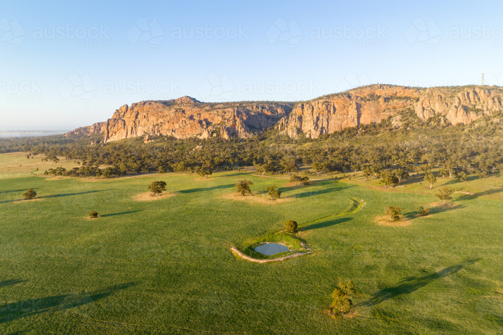 Morning light on Mount Arapiles rising above green farmland and a small dam. - Australian Stock Image