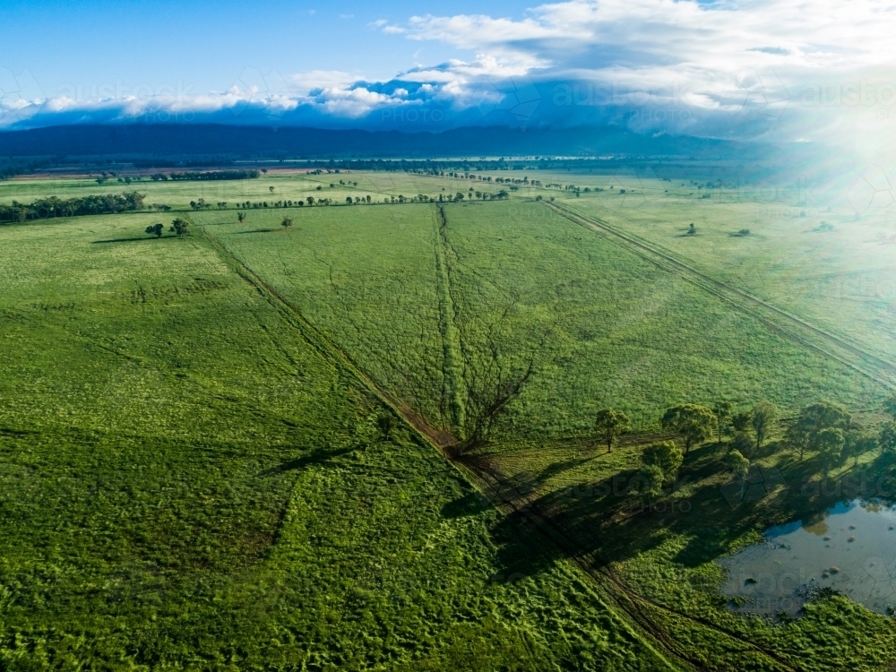 Morning light over green farmland and dam with clouds covering distant hills - Australian Stock Image