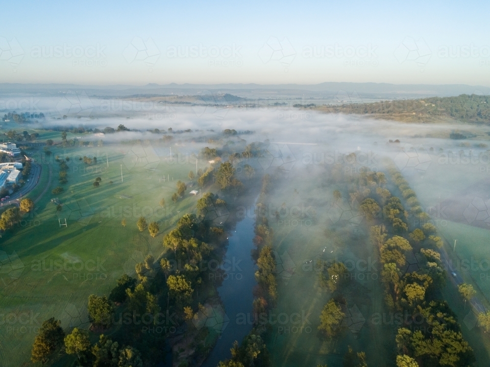 Morning mist covering Hunter River watercourse with green sports field on one side - Australian Stock Image