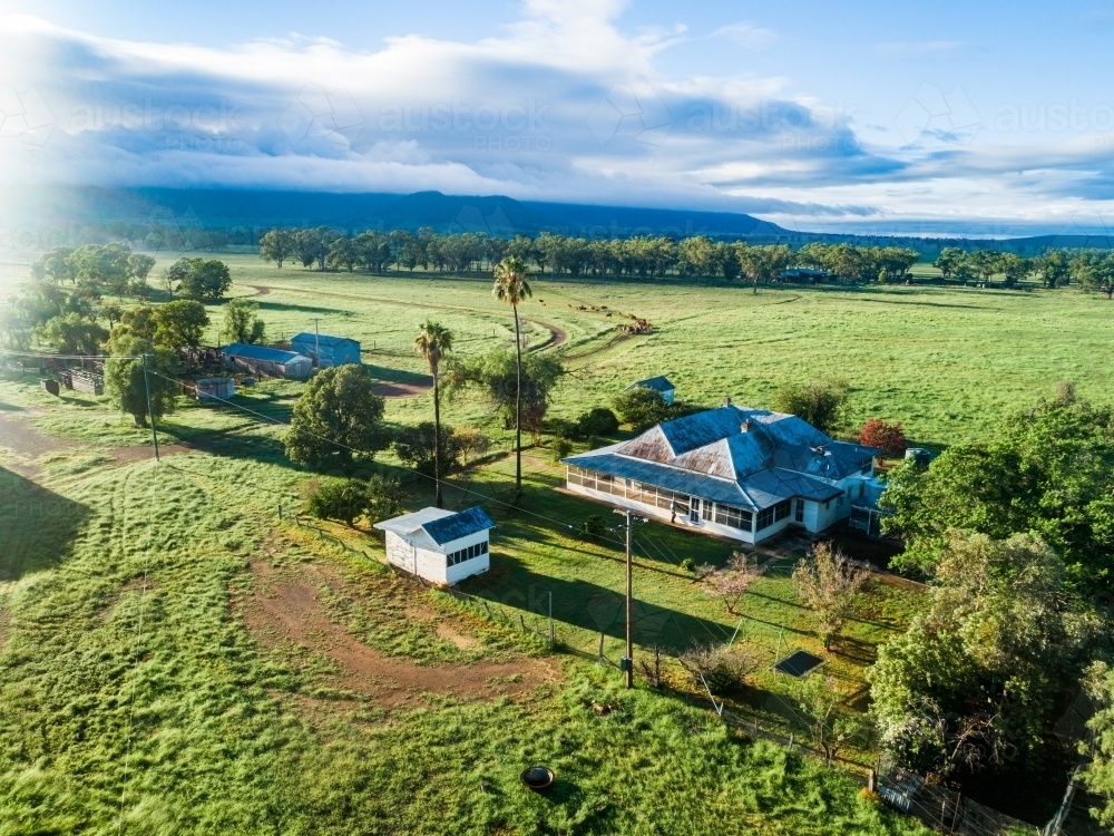Morning sunlight bursting over small country farmstead and green paddocks - Australian Stock Image