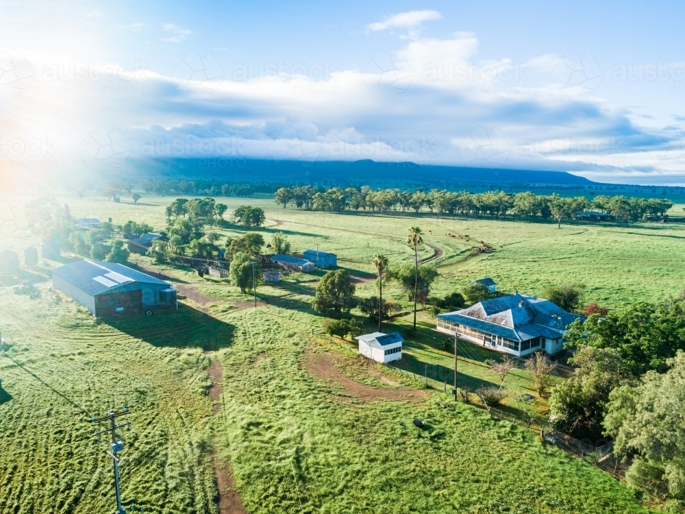 Morning sunlight bursting over small country farmstead and green paddocks - Australian Stock Image