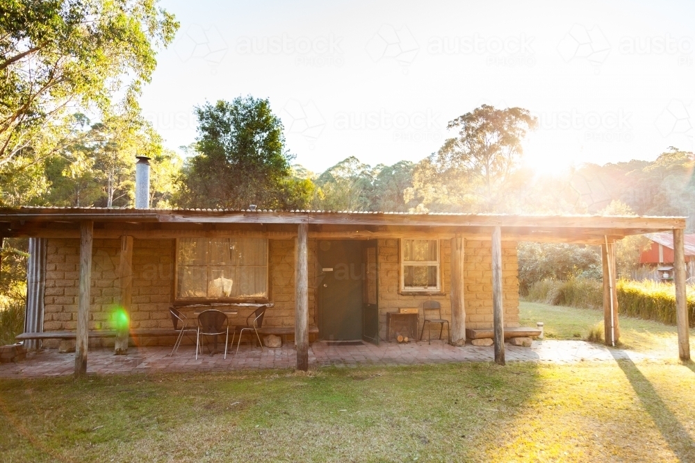 Morning sunlight flare over cottage in clearing - Australian Stock Image
