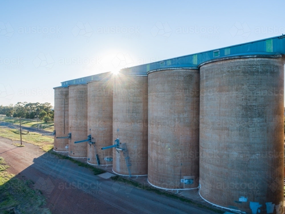 Morning sunlight shining over wheat silo infrastructure beside a train line in the riverina - Australian Stock Image