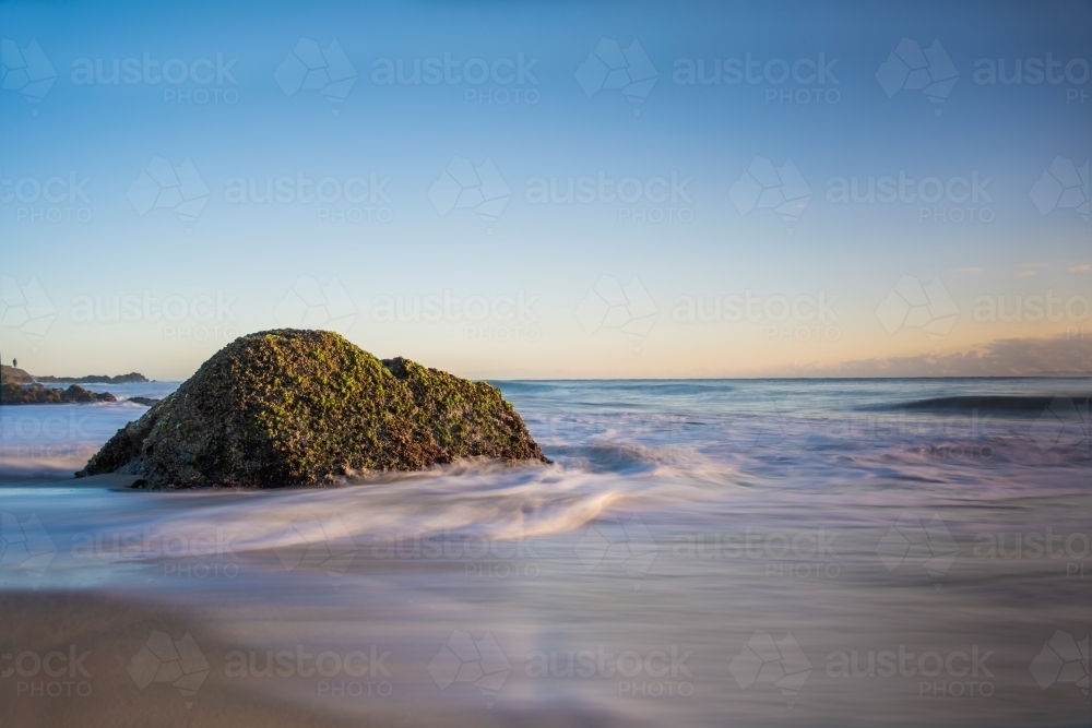 Moss covered stone in the swallow water of the ocean - Australian Stock Image