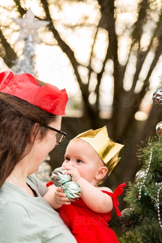 Mother and baby celebrating wearing silly Christmas paper crown hats outside - Australian Stock Image