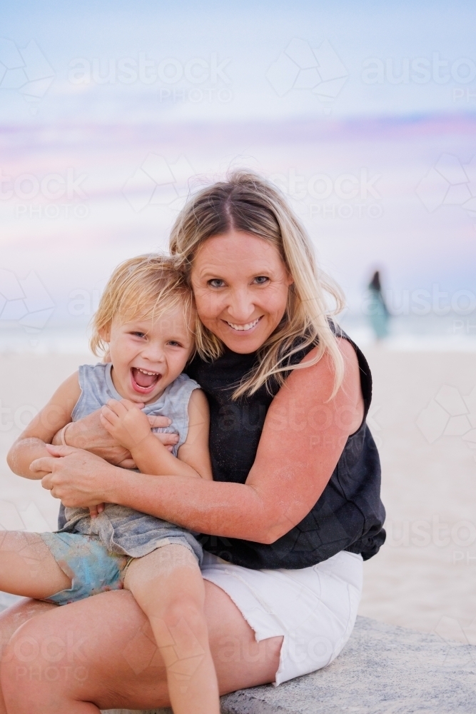 Mother and child embracing on the beach with pink and purple sunset sky - Australian Stock Image