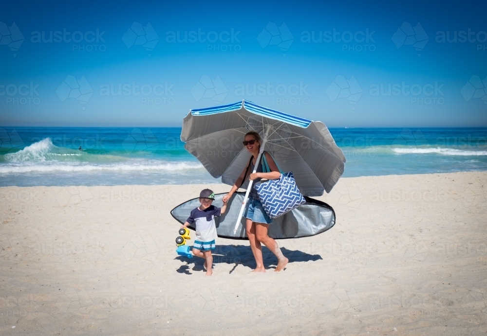 Mother and child walking on beach holding large beach umbrella - Australian Stock Image