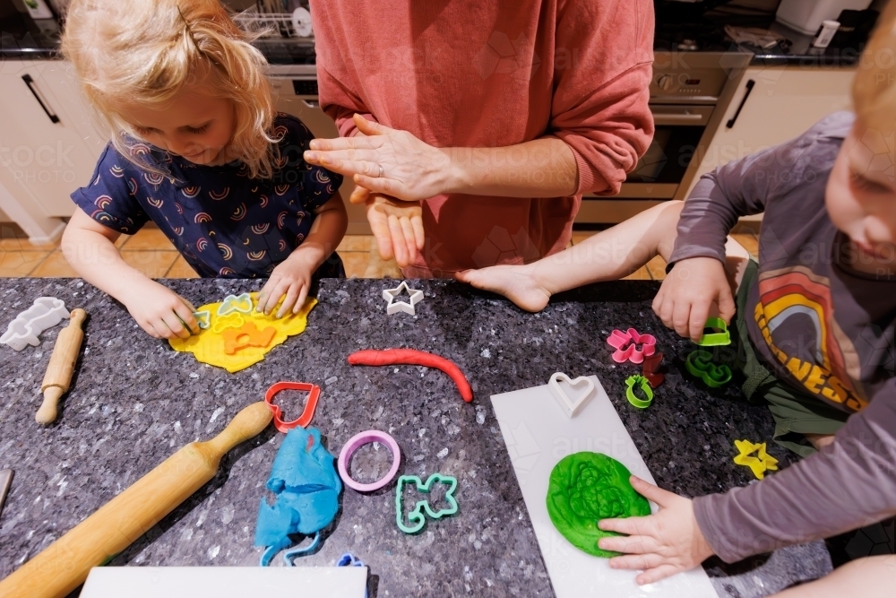 Mother and children playing at home with playdough on kitchen bench - Australian Stock Image