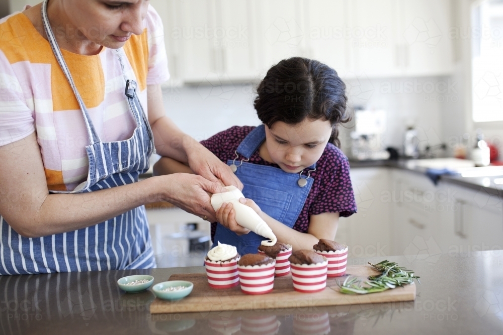 Mother and daughter at home in kitchen decorating cupcakes - Australian Stock Image
