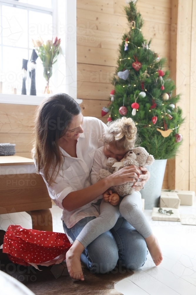 Mother and daughter cuddling with Christmas tree in background - Australian Stock Image