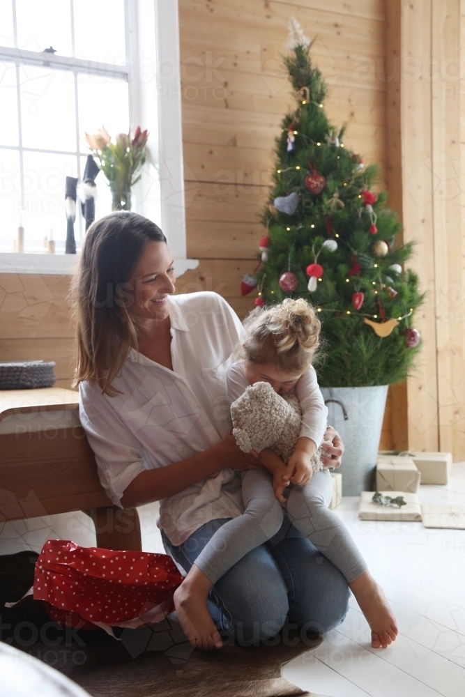 Mother and daughter cuddling with Christmas tree in background - Australian Stock Image
