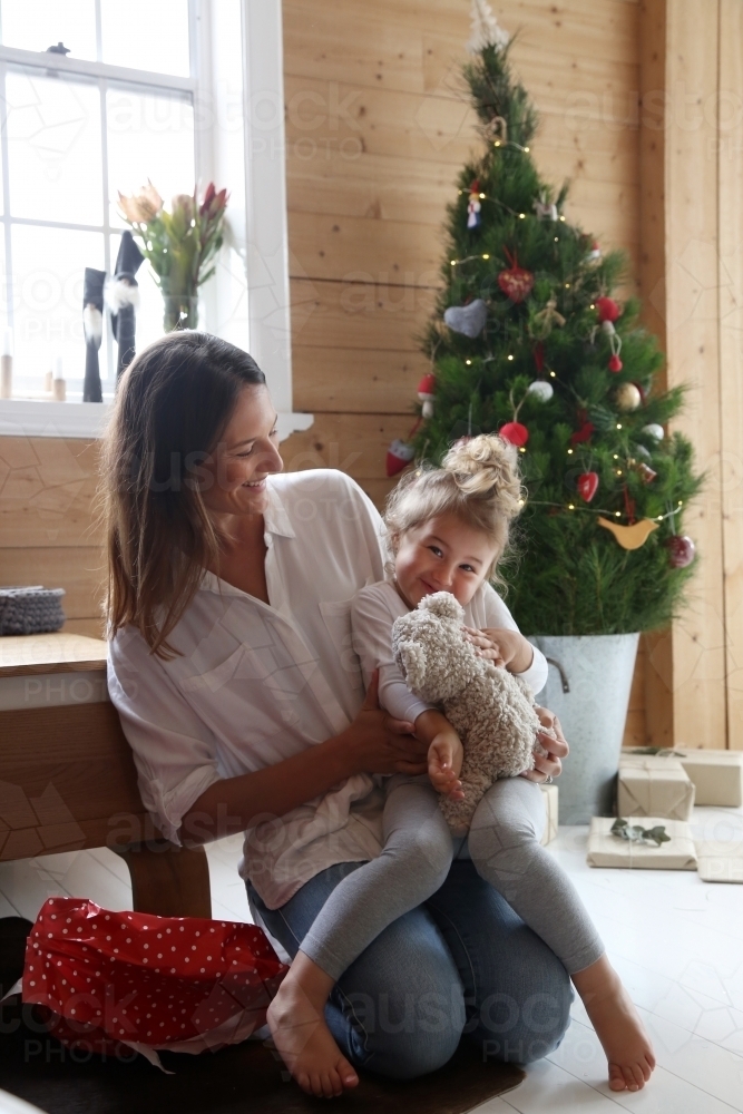 Mother and daughter cuddling with Christmas tree in background - Australian Stock Image