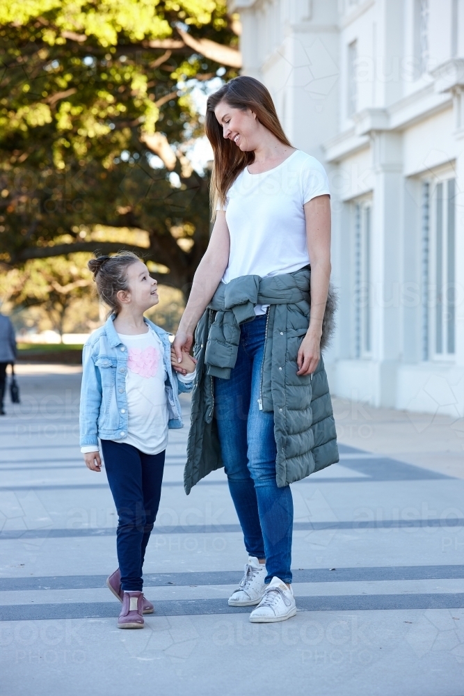 Mother and daughter holding hands walking on beach promenade - Australian Stock Image
