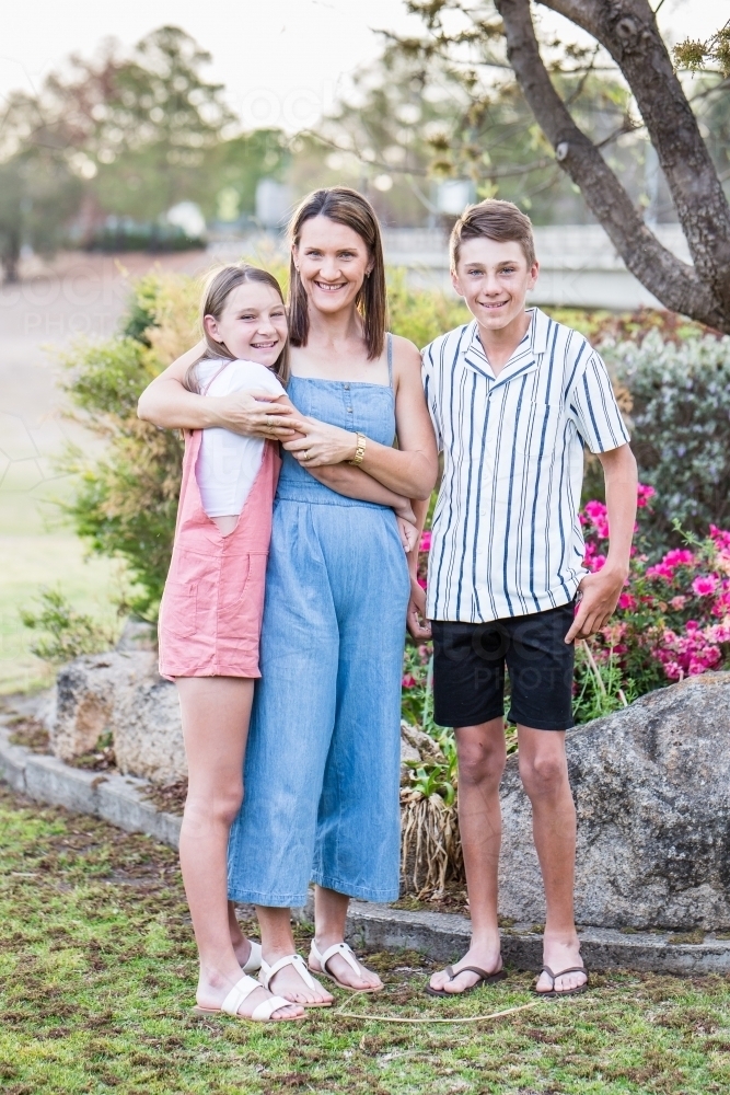 Mother and daughter hugging standing with son - Australian Stock Image