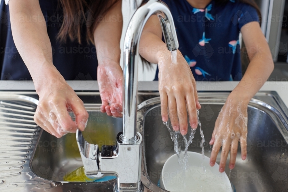 Mother and daughter in kitchen washing hands - Australian Stock Image