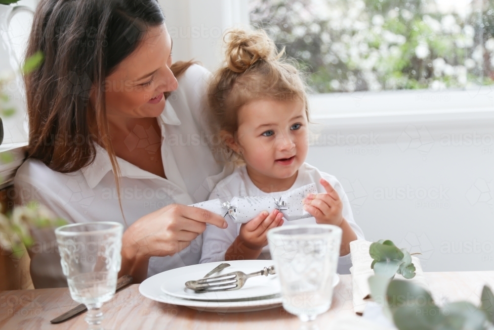 Mother and daughter opening bon bon at dining table - Australian Stock Image