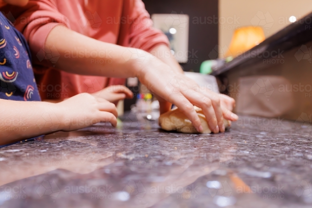 Mother and daughter's hands kneading dough on kitchen bench - Australian Stock Image