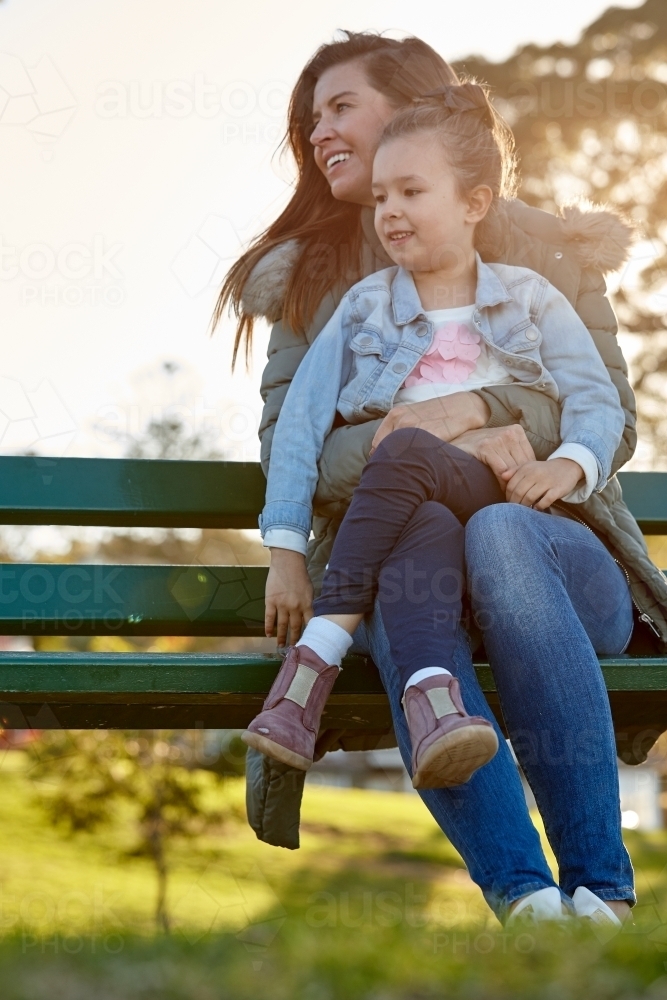 Mother and daughter sharing time laughing at park bench - Australian Stock Image