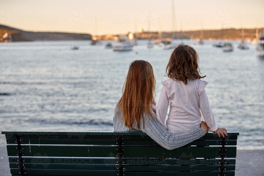 Mother and daughter sitting on park bench at park on sunset - Australian Stock Image