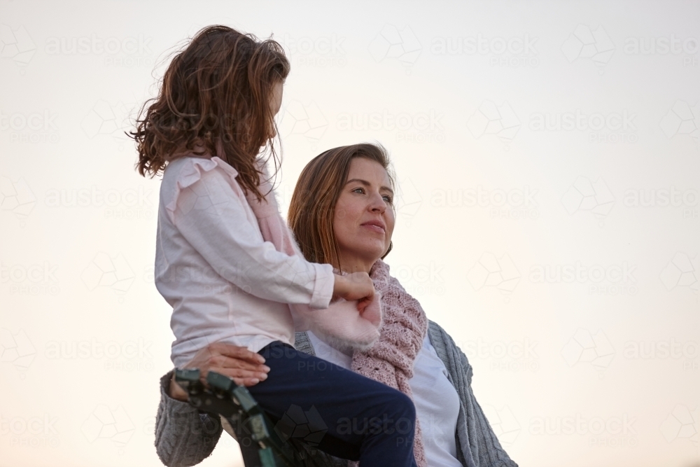 Mother and daughter sitting on park bench at park on sunset - Australian Stock Image