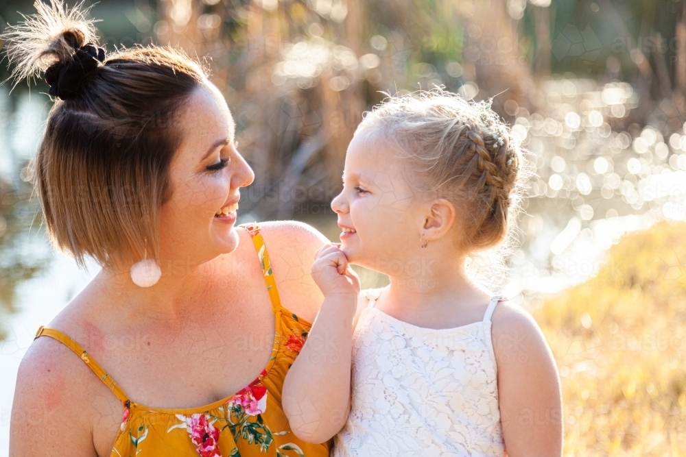 Mother and daughter smile at one another outside - Australian Stock Image