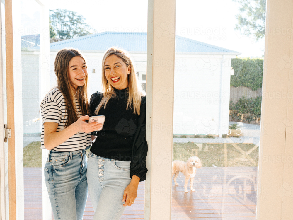 Mother and daughter standing in the doorway smiling. - Australian Stock Image