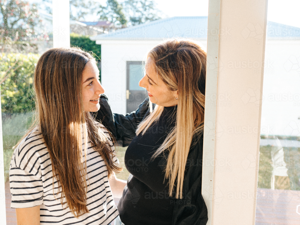 Mother and daughter standing in the doorway smiling while looking at each other. - Australian Stock Image