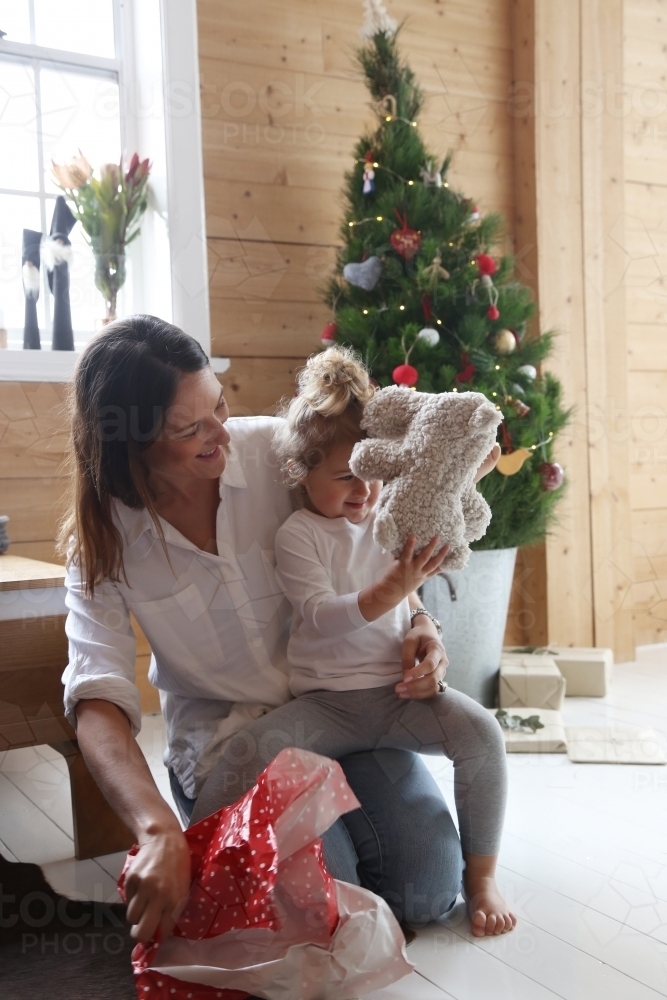 Mother and daughter unwrapping present with Christmas tree in background - Australian Stock Image