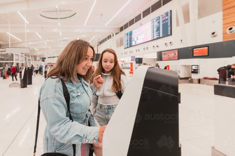 Mother and daughter using self-serve kiosk to check in for flight at the airport - Australian Stock Image