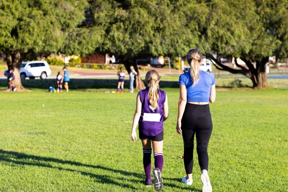 mother and daughter walking away off football oval with daughter in footy kit after the game - Australian Stock Image