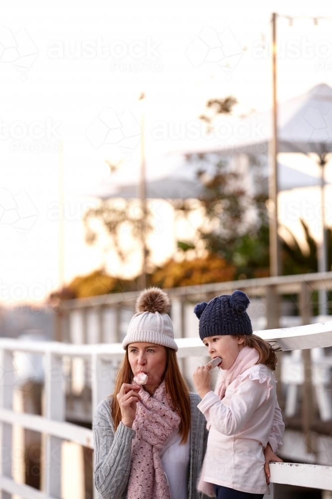 Mother and daughter wearing beanies on wharf eating ice creams : Austockphoto Mother and daughter wearing beanies on wharf eating ice creams - Australian Stock Image
