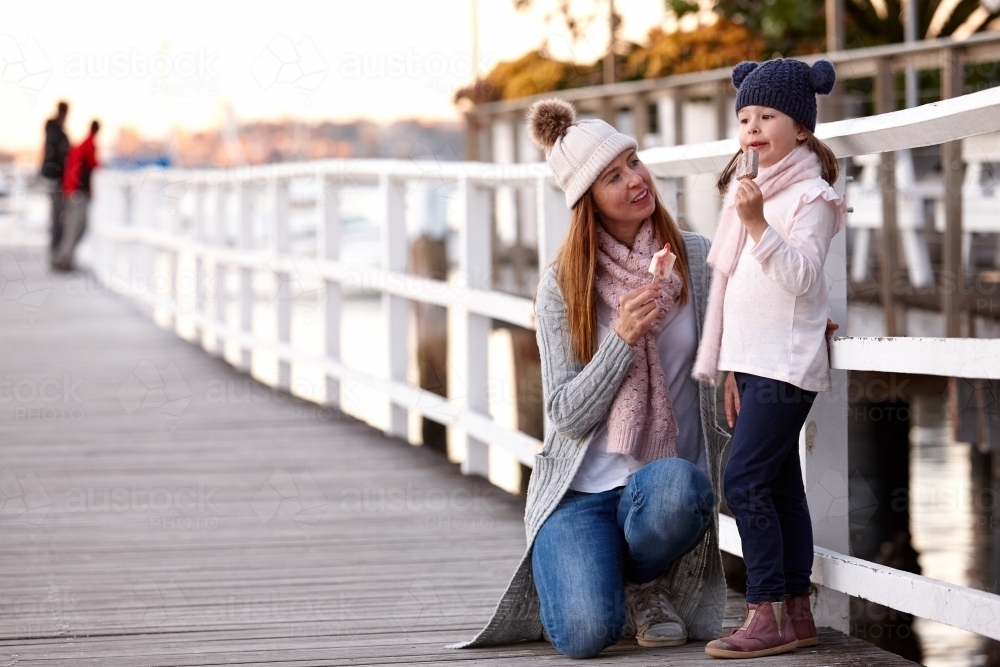 Mother and daughter wearing beanies on wharf eating ice creams - Australian Stock Image
