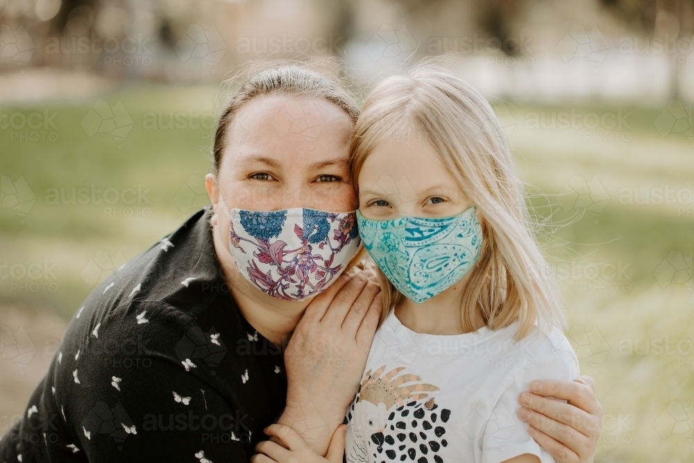 Mother and daughter wearing fabric masks during the corona virus COVID-19 pandemic hugging outside - Australian Stock Image