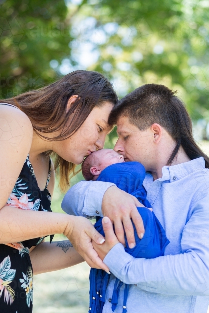 Mother and Father holding their baby boy together and kissing him - Australian Stock Image