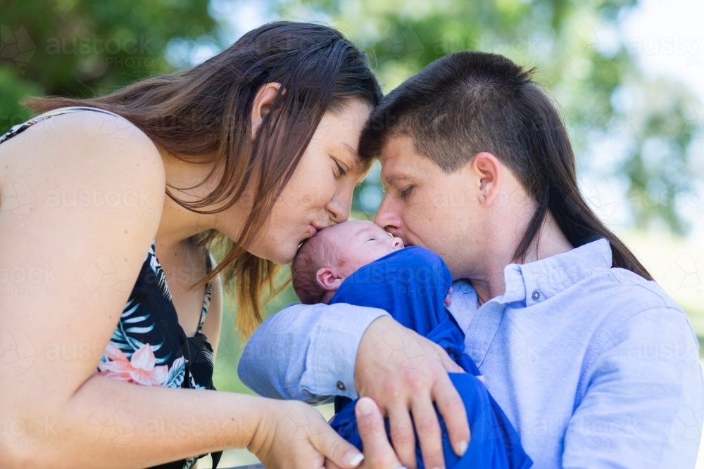 Mother and father holding their newborn child and kissing him - Australian Stock Image