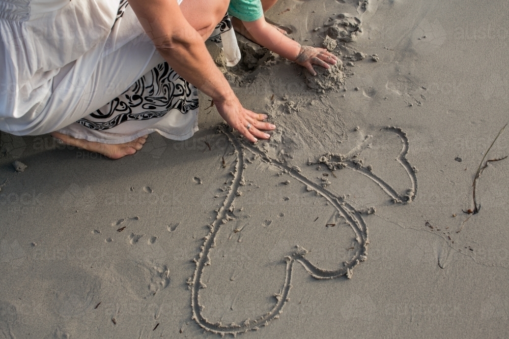 Mother and son drawing love hearts in the sand - Australian Stock Image