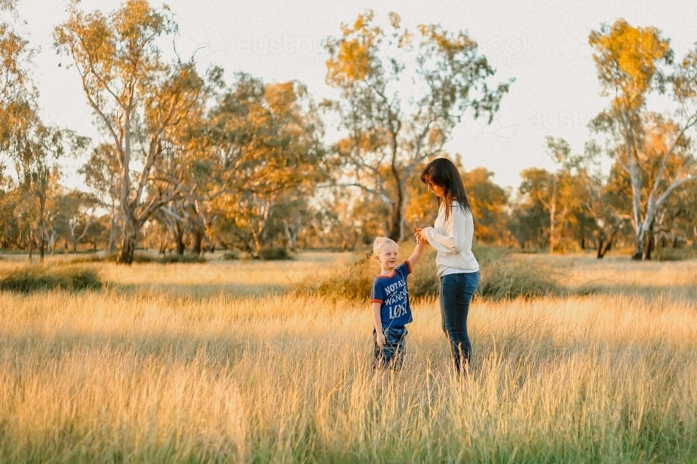 Mother and son standing in field with with long grass at sunset - Australian Stock Image
