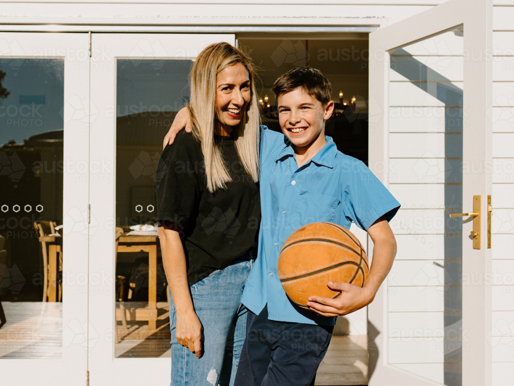 Mother and son standing outside the house holding a basketball. - Australian Stock Image