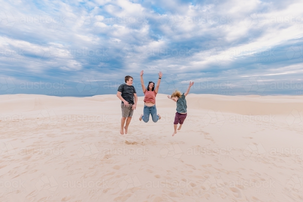 Mother and sons jumping for joy on the sand dunes of Stockton Beach - Australian Stock Image