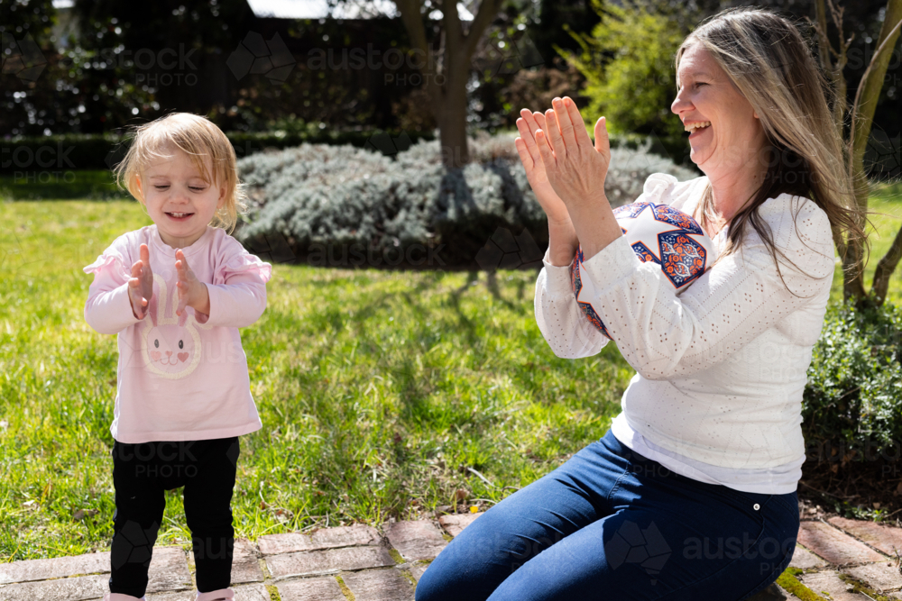 Mother and toddler daughter clapping hands together in the garden - Australian Stock Image