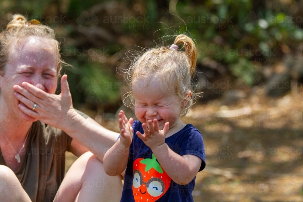 Mother and toddler daughter laughing hysterically in backyard. - Australian Stock Image