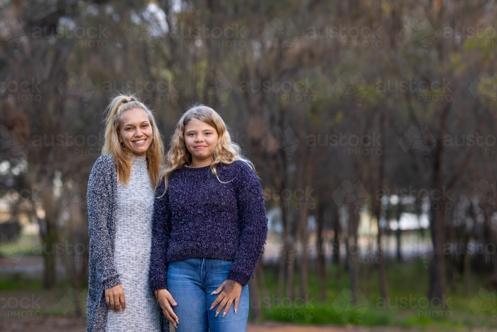 mother and tween daughter standing together outdoors near trees - Australian Stock Image