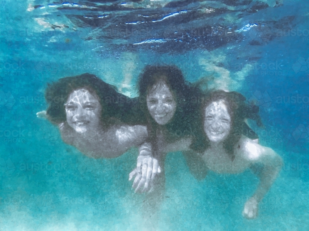 Mother and two boys playing together in ocean on calm day - Australian Stock Image