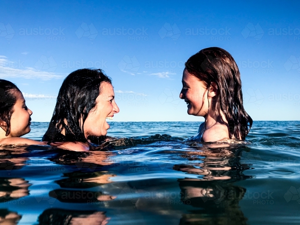 Mother and two boys playing together in ocean on calm day - Australian Stock Image