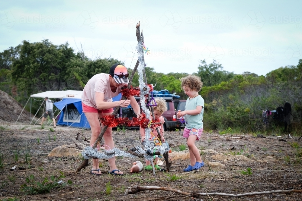 Mother and two children decorating camp Christmas tree on rural property with camper van - Australian Stock Image